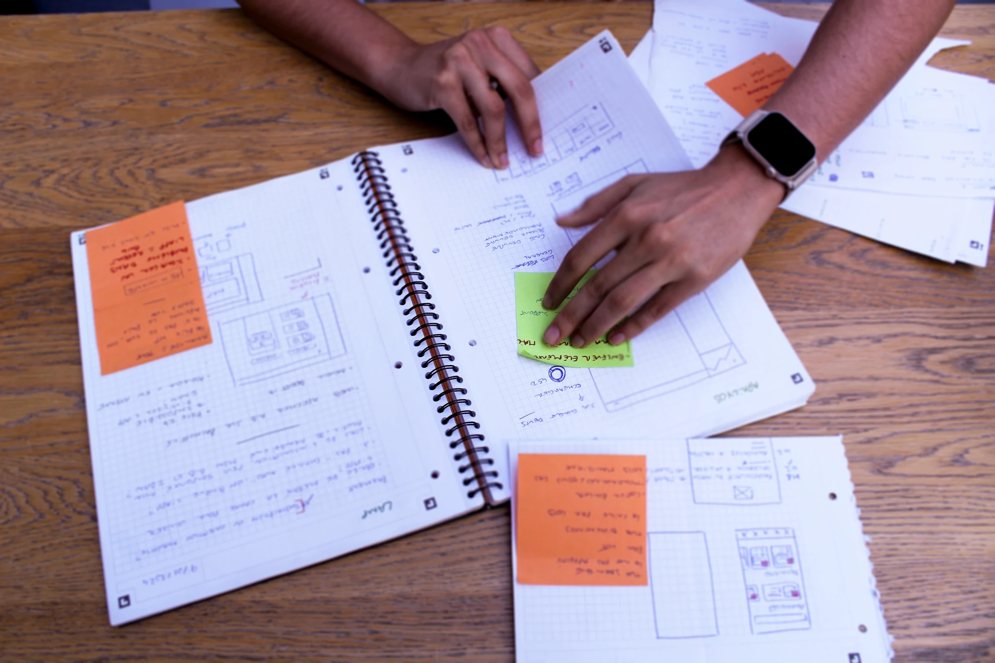 Des mains annotent un carnet de croquis d’interfaces couvert de pense-bêtes